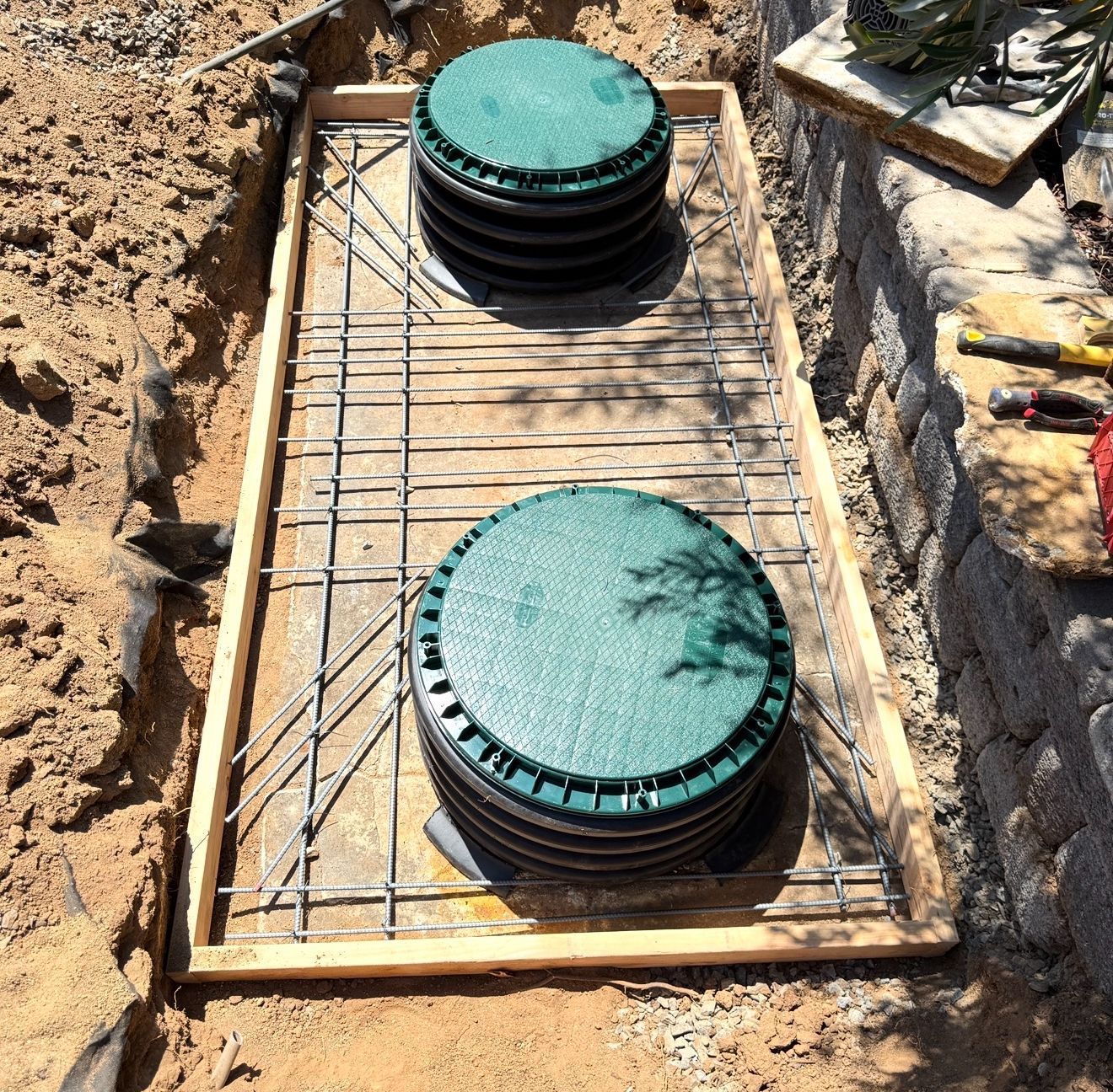 Two green-lidded utility access covers set in a rebar-lined concrete trench