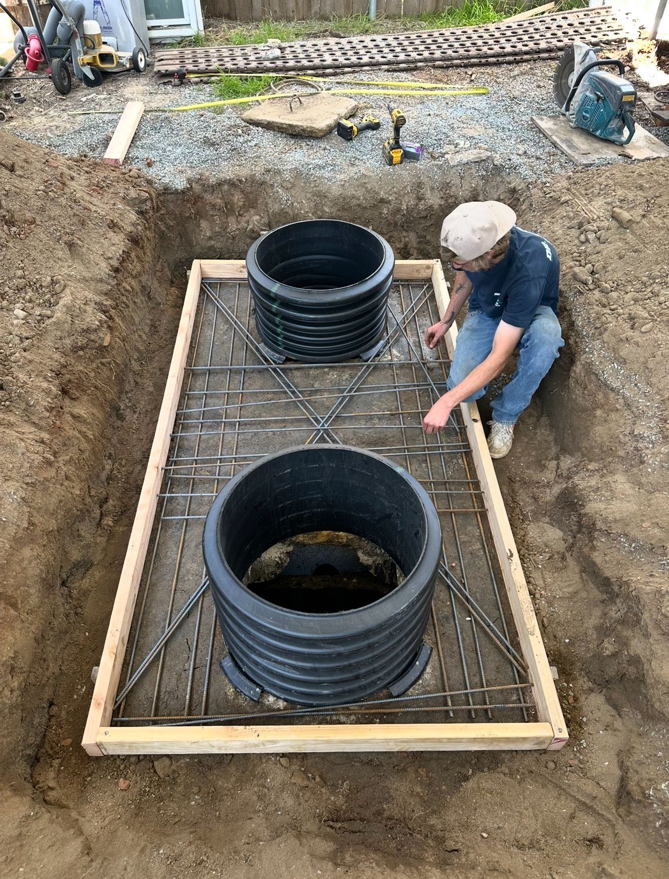 Worker installing drainage pipes in a gravel trench with rebar and wooden framing