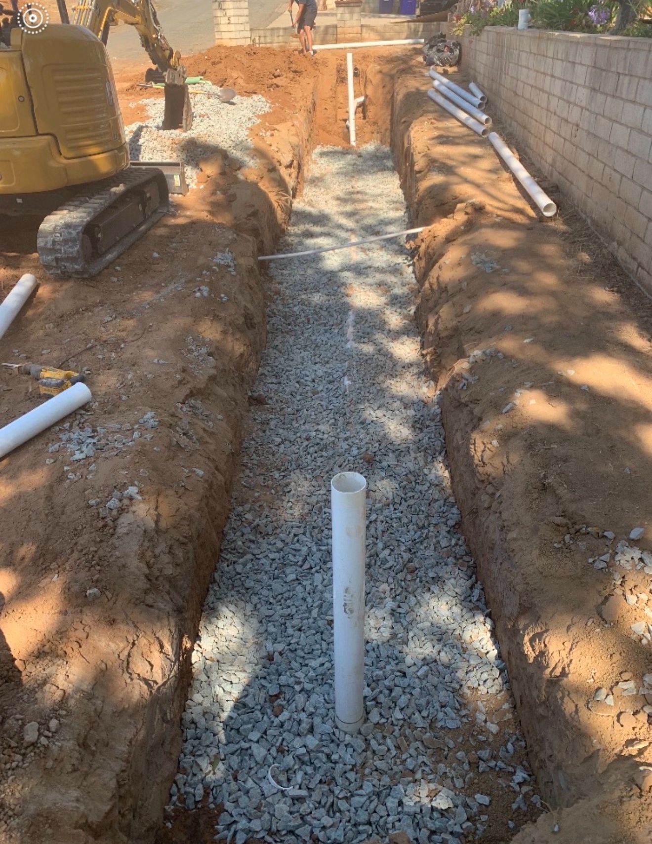 Construction trench with gravel base and white PVC pipes along a block wall