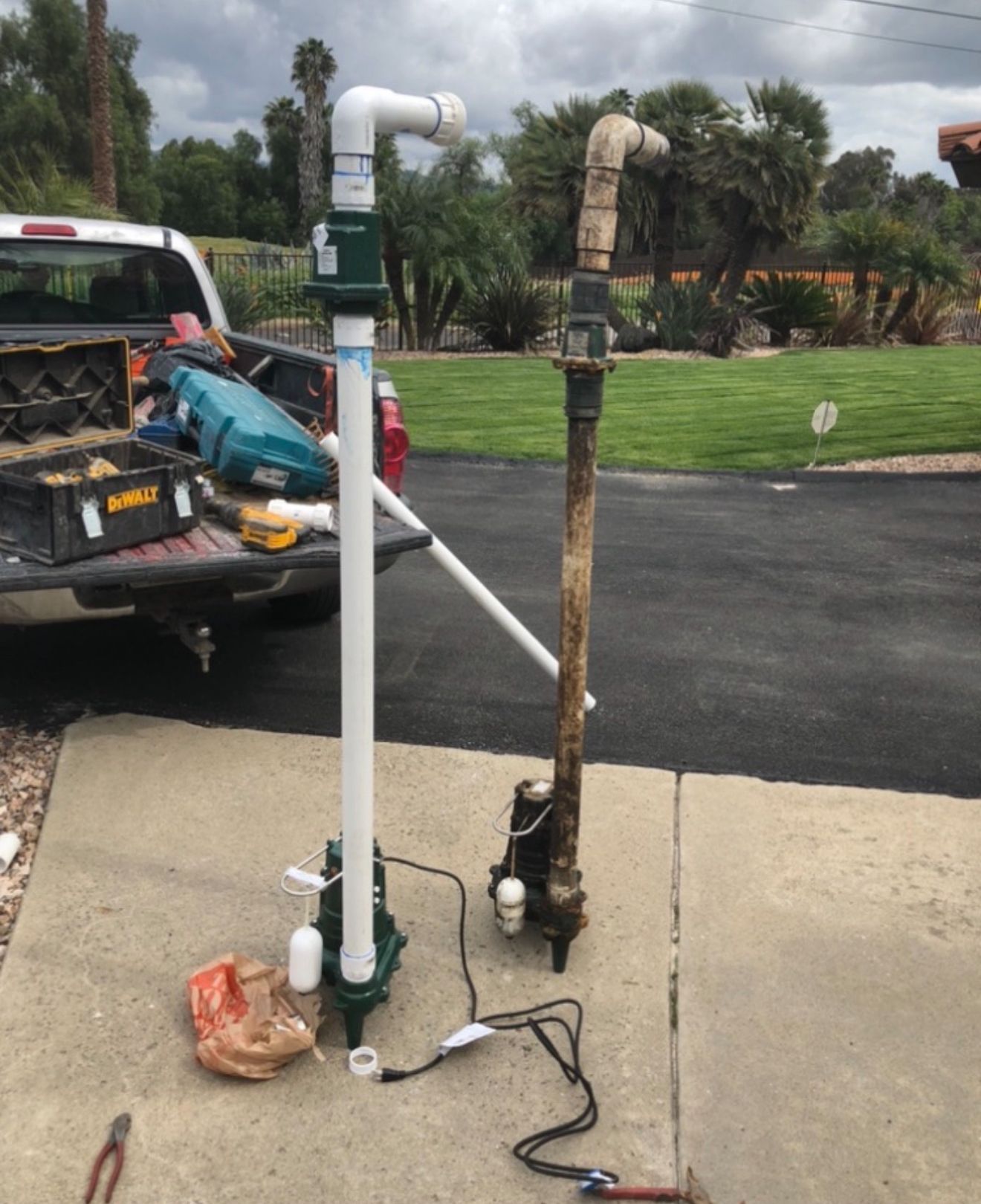 Broken pipes beside a driveway, with one white and one rusted vertical pipe near a truck.