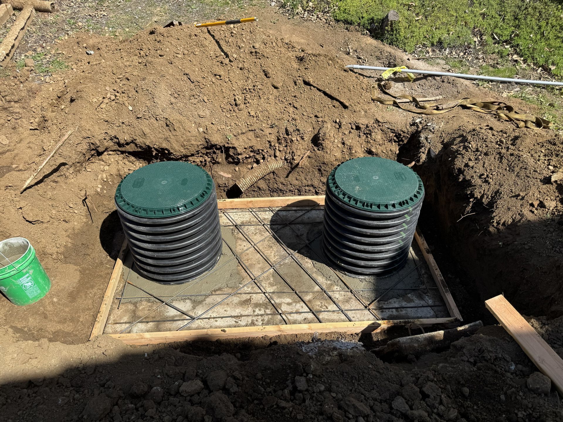 Two black utility access covers installed in a dug trench beside a mound of dirt.