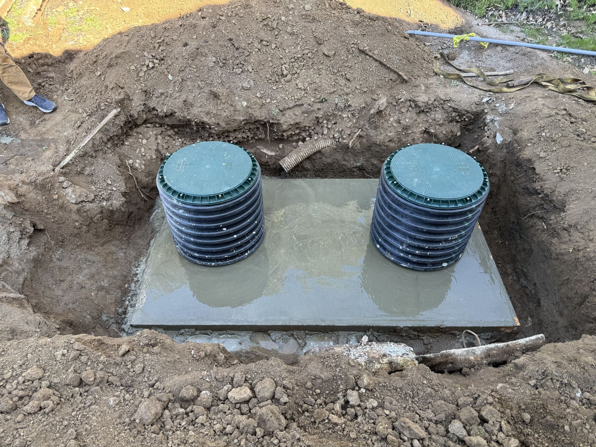 Two black cylindrical tanks on a concrete slab in an excavated dirt pit