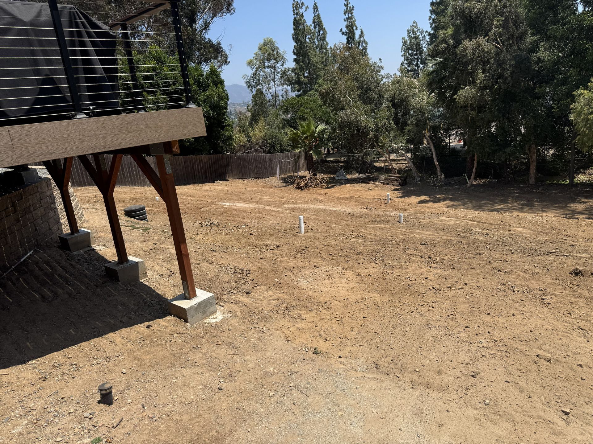 Backyard with dry dirt ground, trees, and a raised deck on the left side