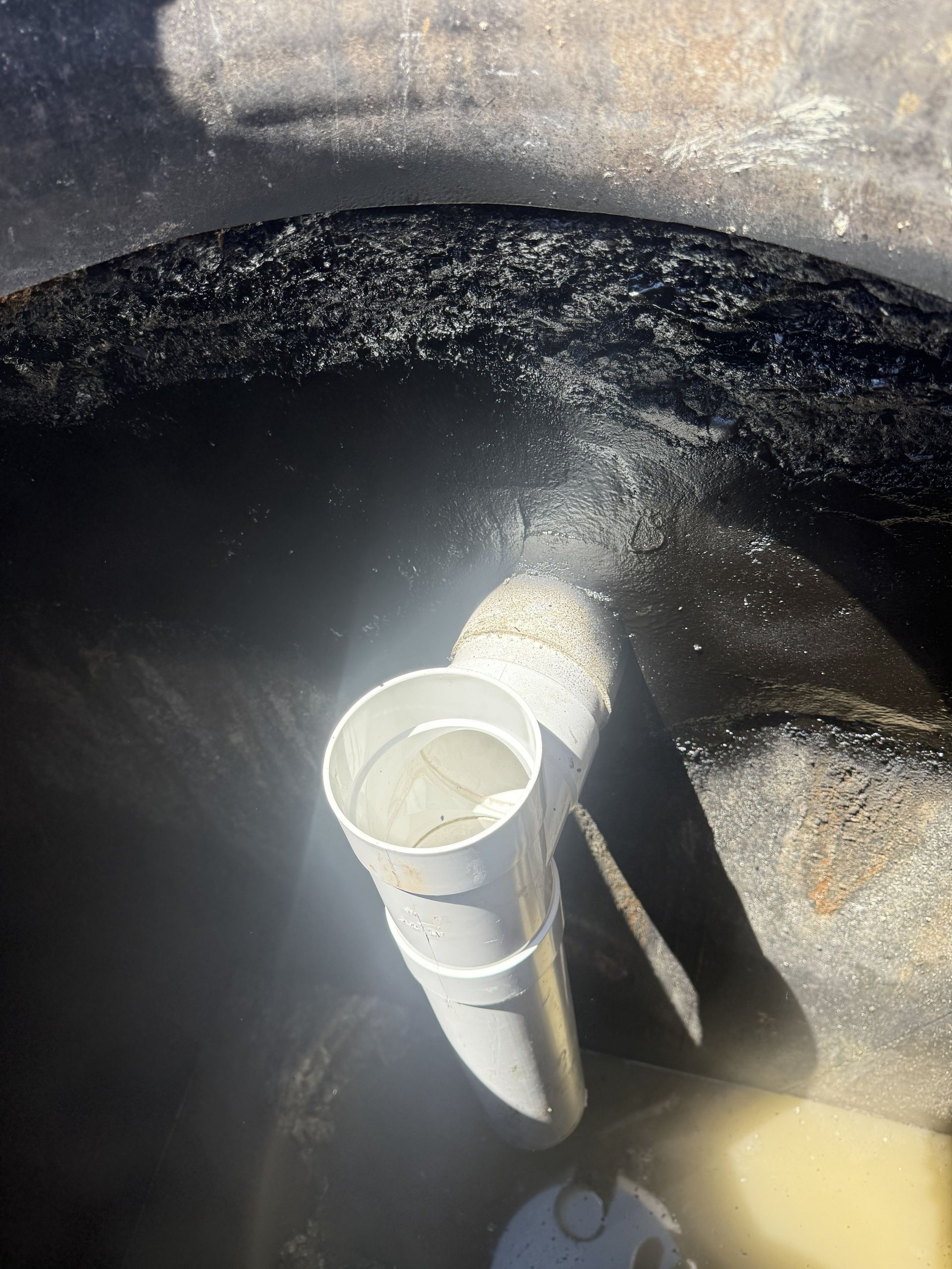 White PVC pipe inside a dark tank, with cloudy liquid or residue around it.