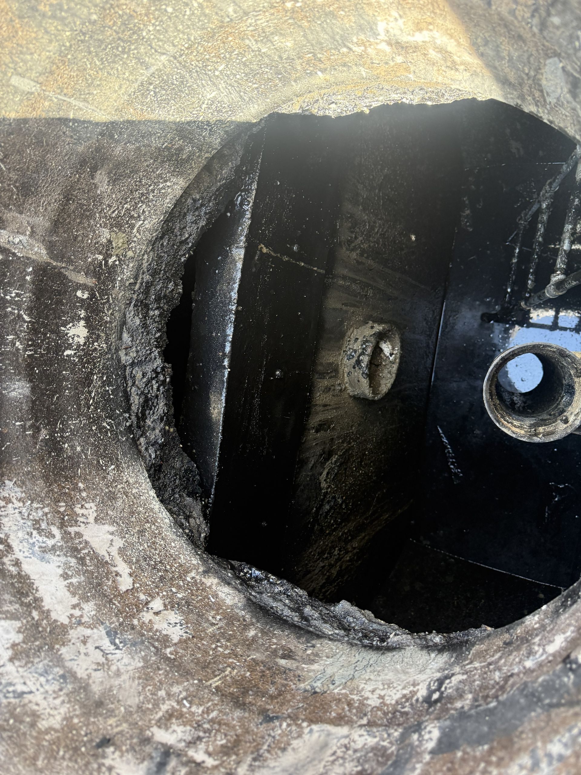 Close-up of a dark circular metal pipe or tank opening with rust and grime around the rim.
