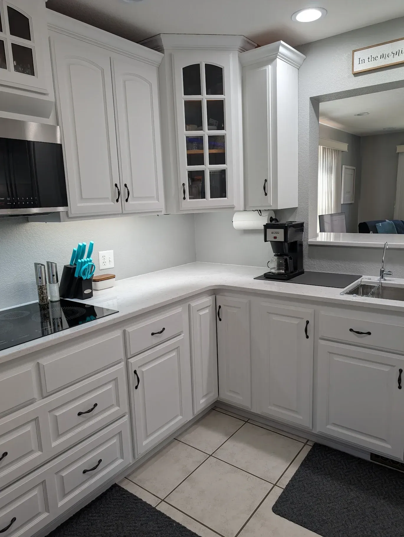 A kitchen with white cabinets , a sink , a stove , and a microwave.