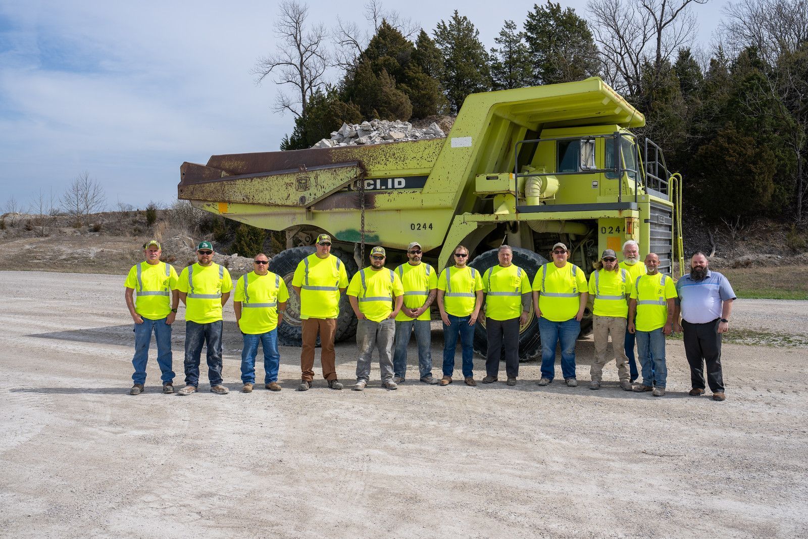 a group of construction workers are posing for a picture in front of a dump truck .