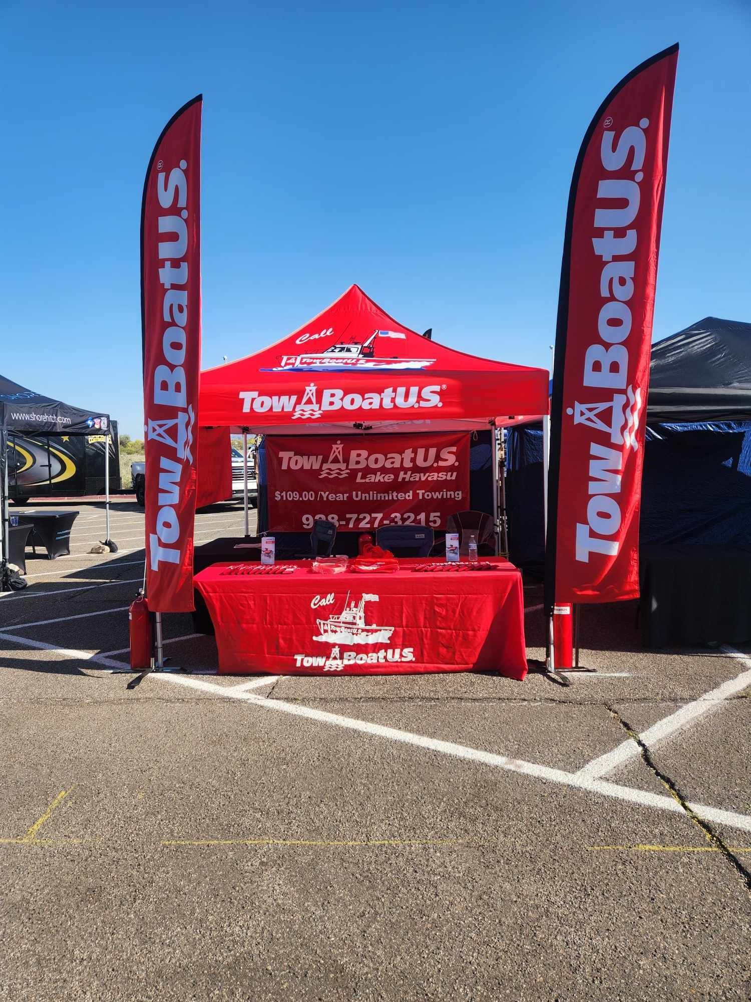 Red TowBoatUS booth with flags at an outdoor event on a sunny day.