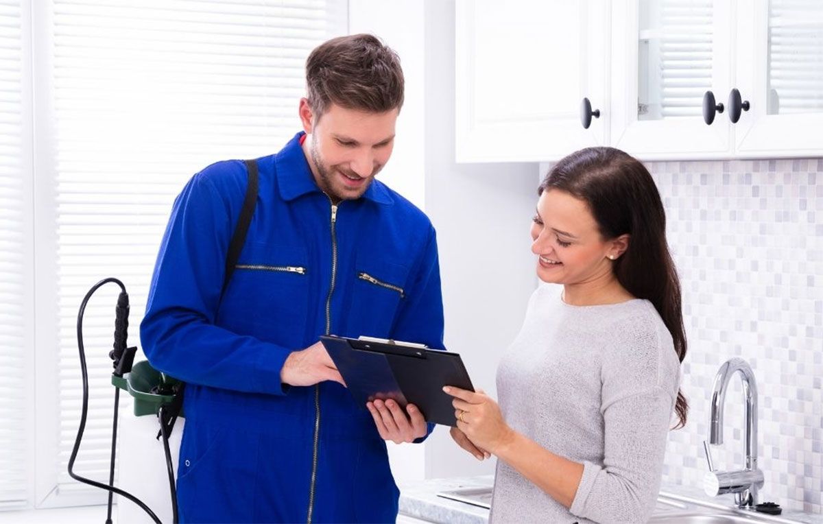 Two people reviewing a tablet in a bright kitchen, one in a blue work suit, both smiling.