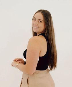 A woman with long hair is wearing a black tank top and tan shorts.