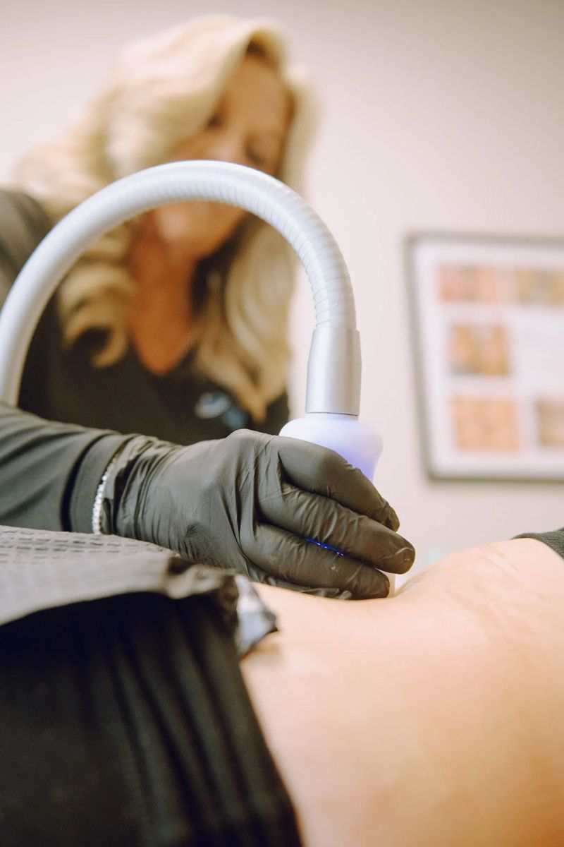 A person receiving a body contouring treatment. A gloved hand holds a device emitting blue light on a thigh.