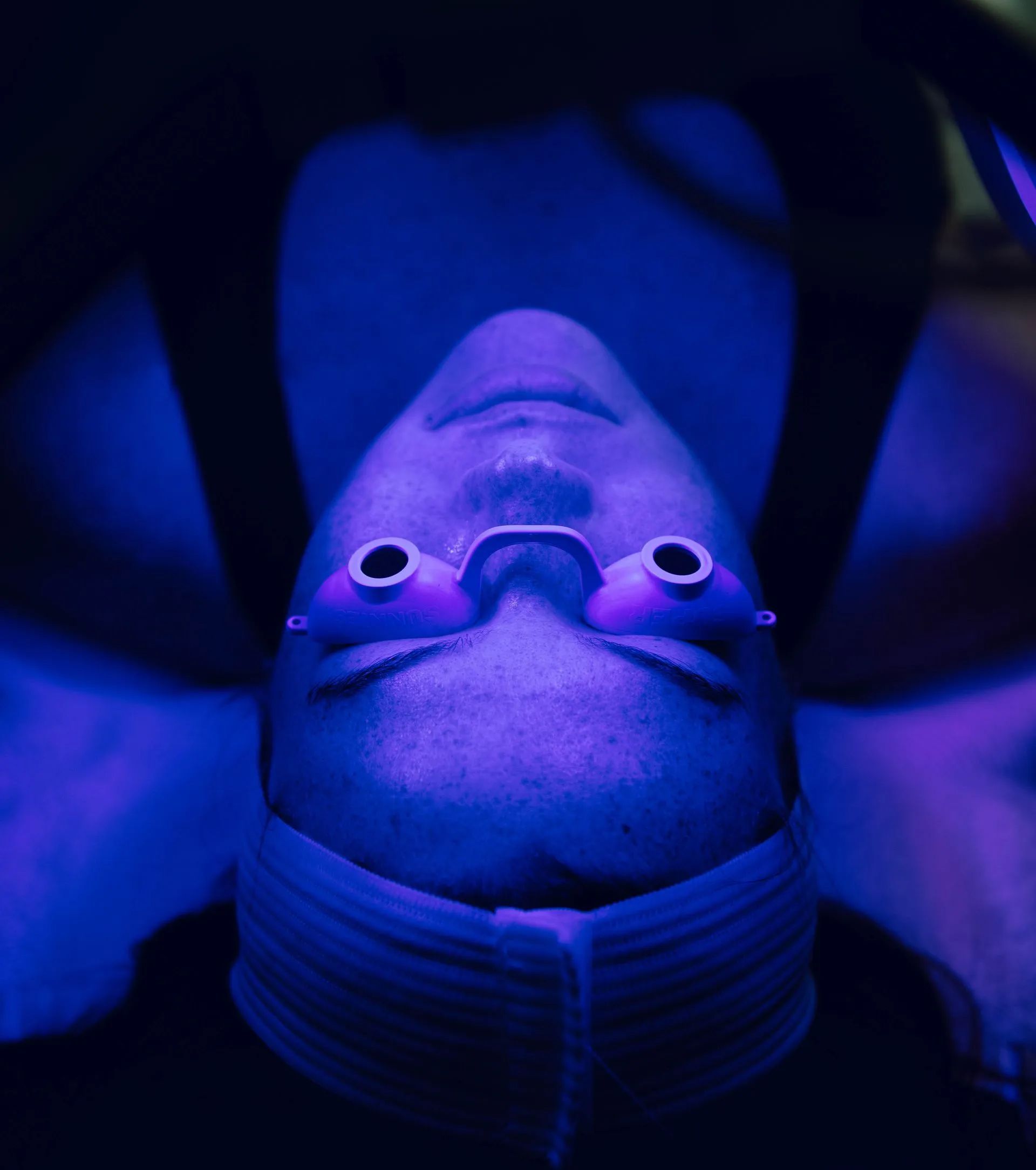 Person wearing protective eyewear under blue light during a skincare treatment.