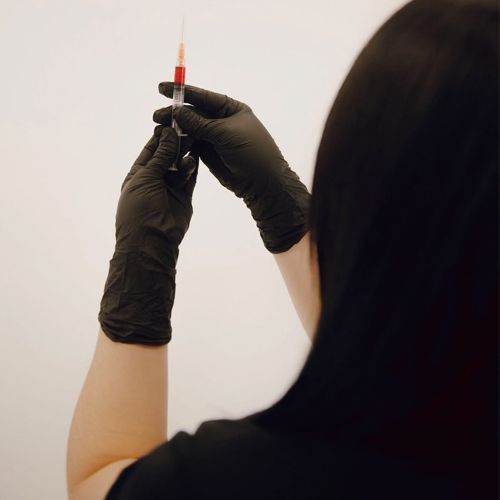 Person wearing black gloves holding a syringe filled with red liquid, preparing for an injection.