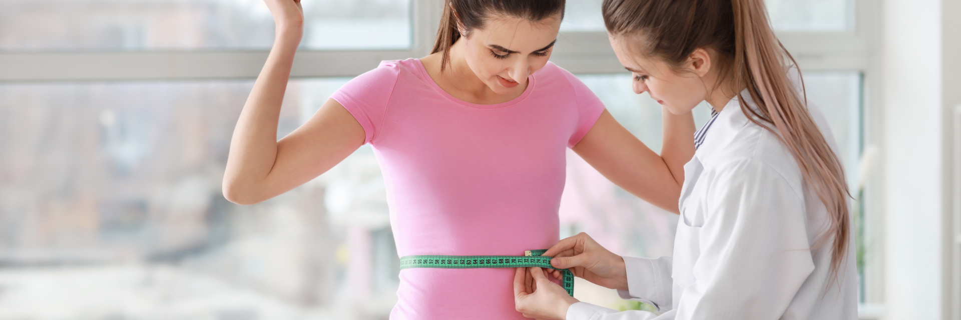 Woman in pink shirt has waist measured by a doctor in a white coat; she looks surprised, raising arms.