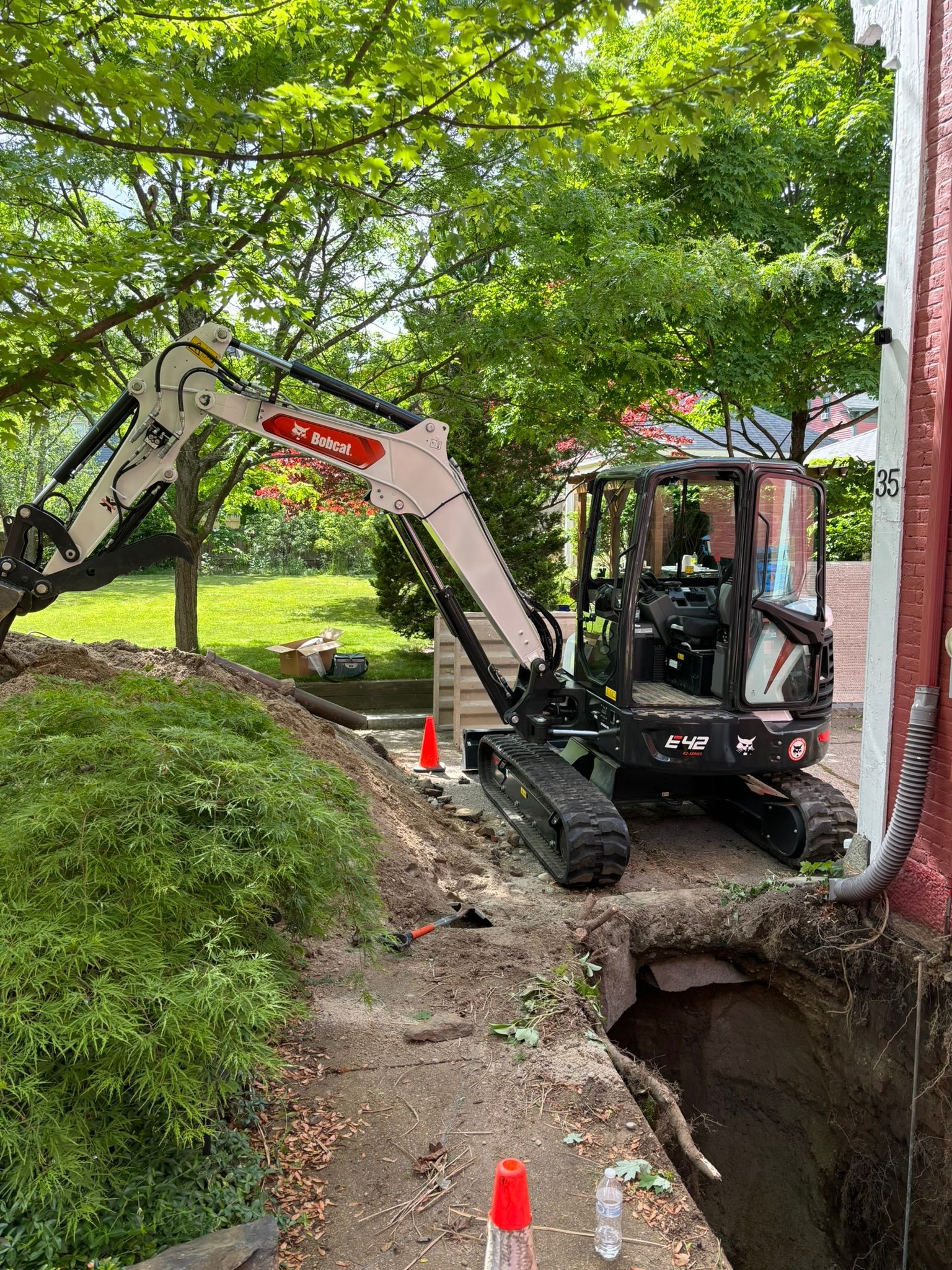 A bobcat excavator is digging a hole in the ground next to a house.
