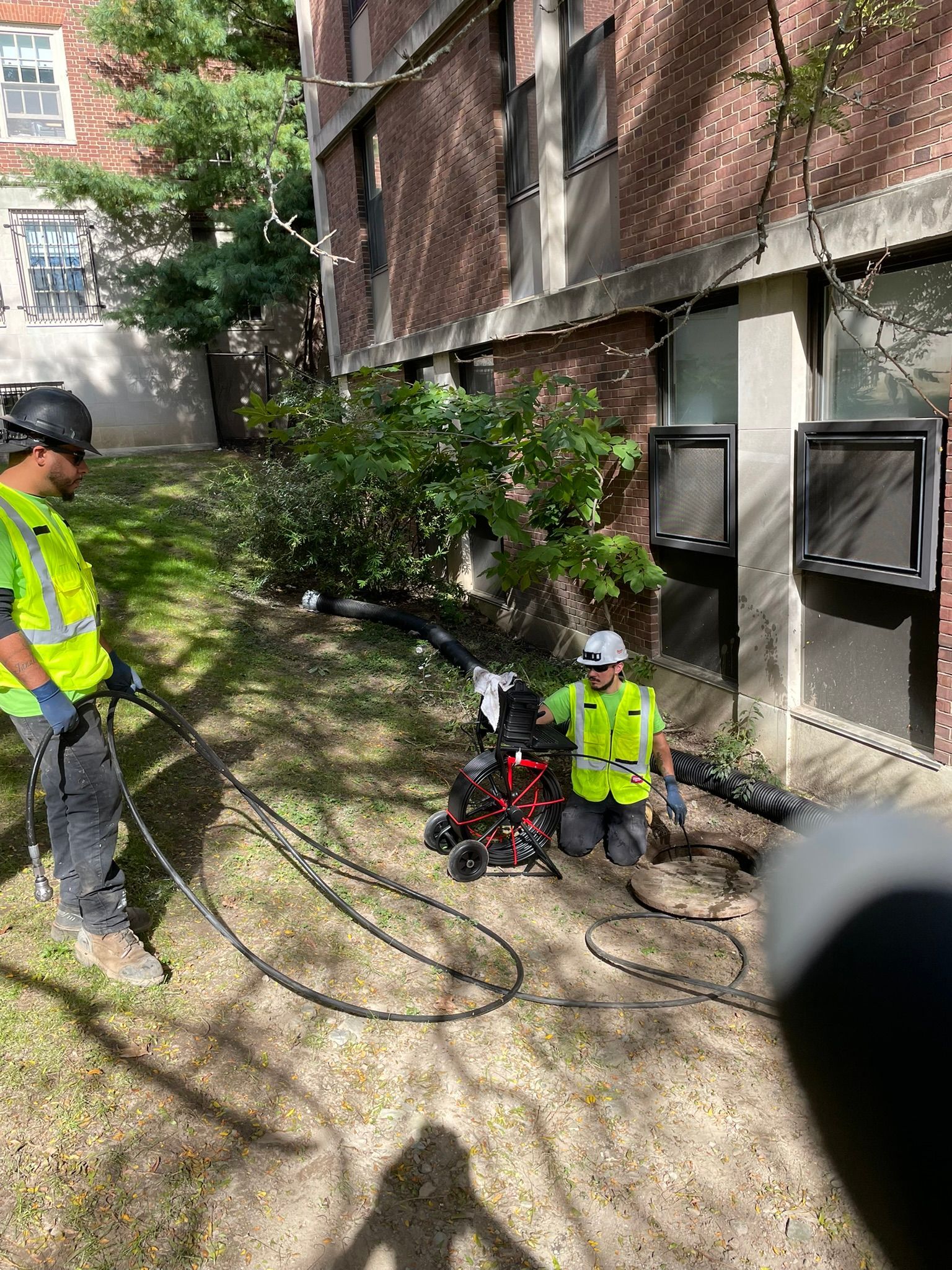 Two men are working on a drain in front of a building.