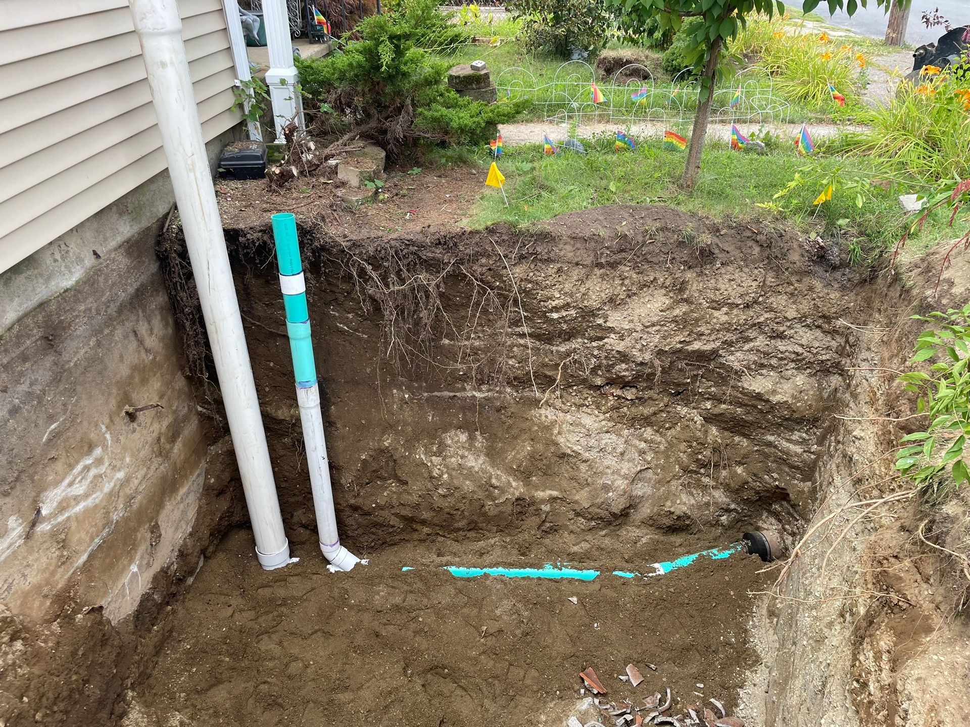 A hole in the ground next to a house with pipes in it.