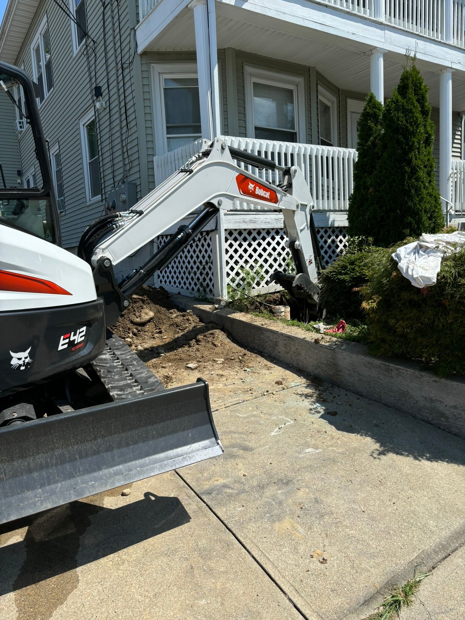 A bobcat excavator is sitting on the sidewalk in front of a house.