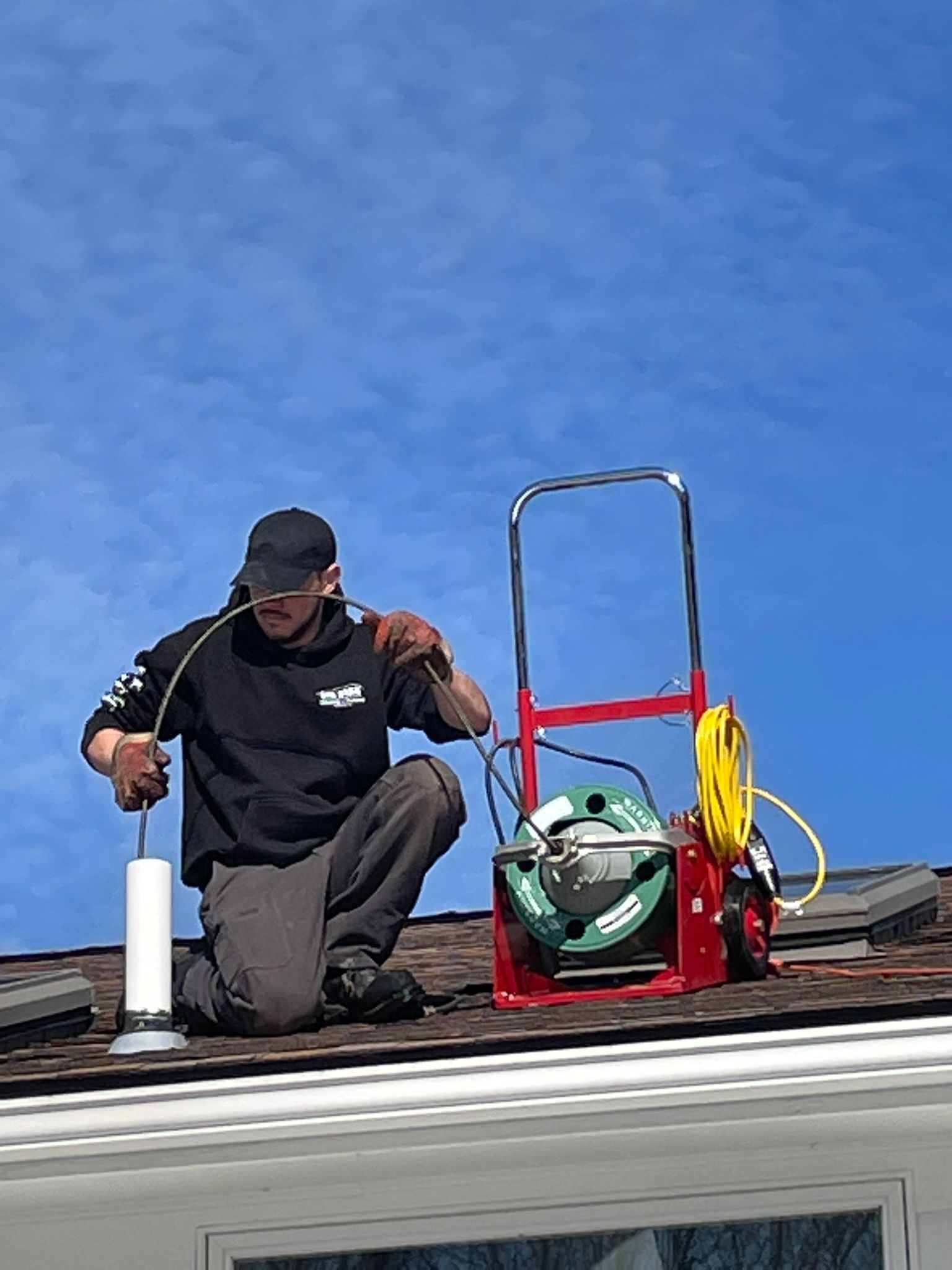 A man is kneeling on top of a roof with a hose.