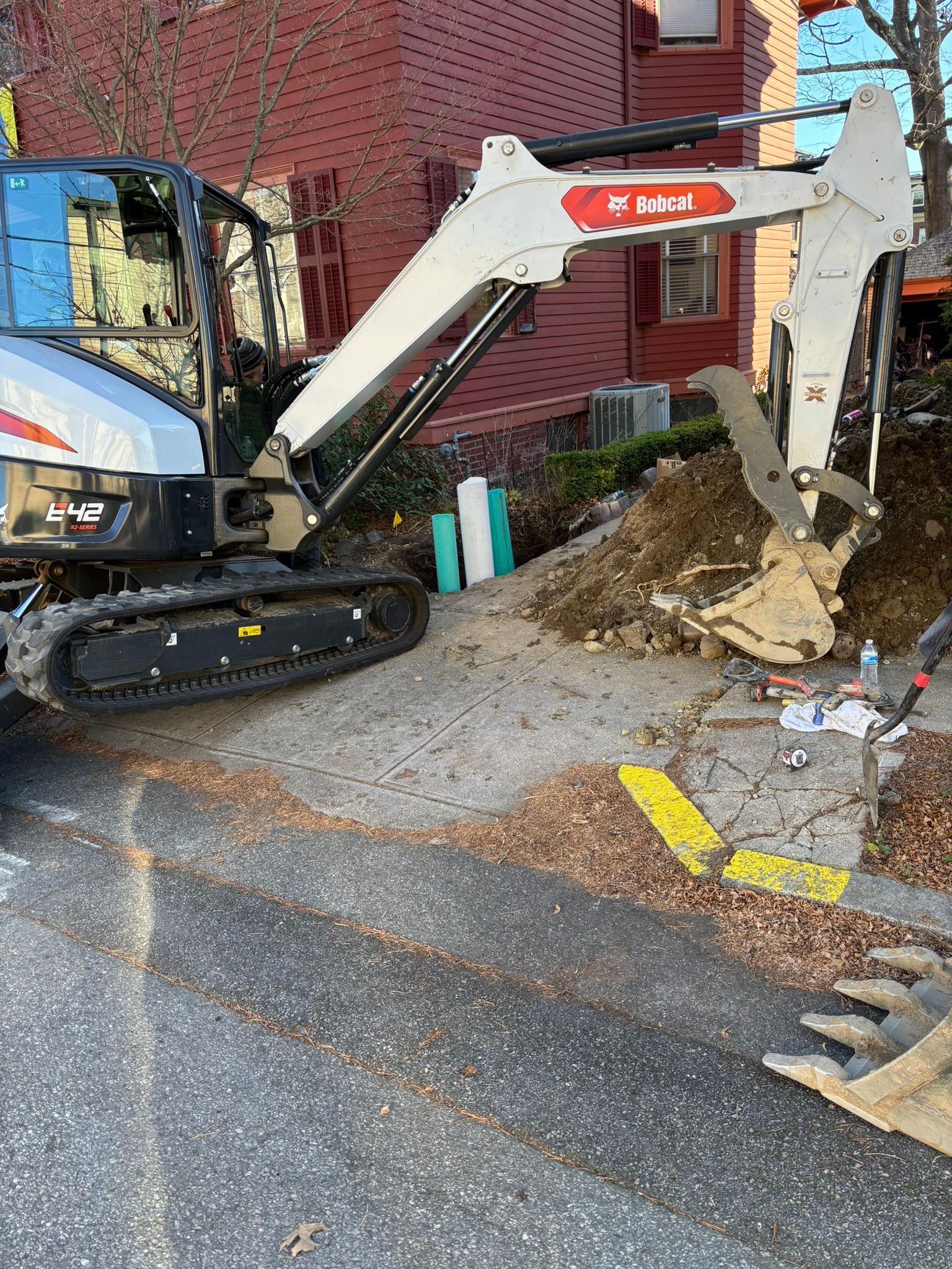 A small excavator is digging a hole in the ground in front of a building.