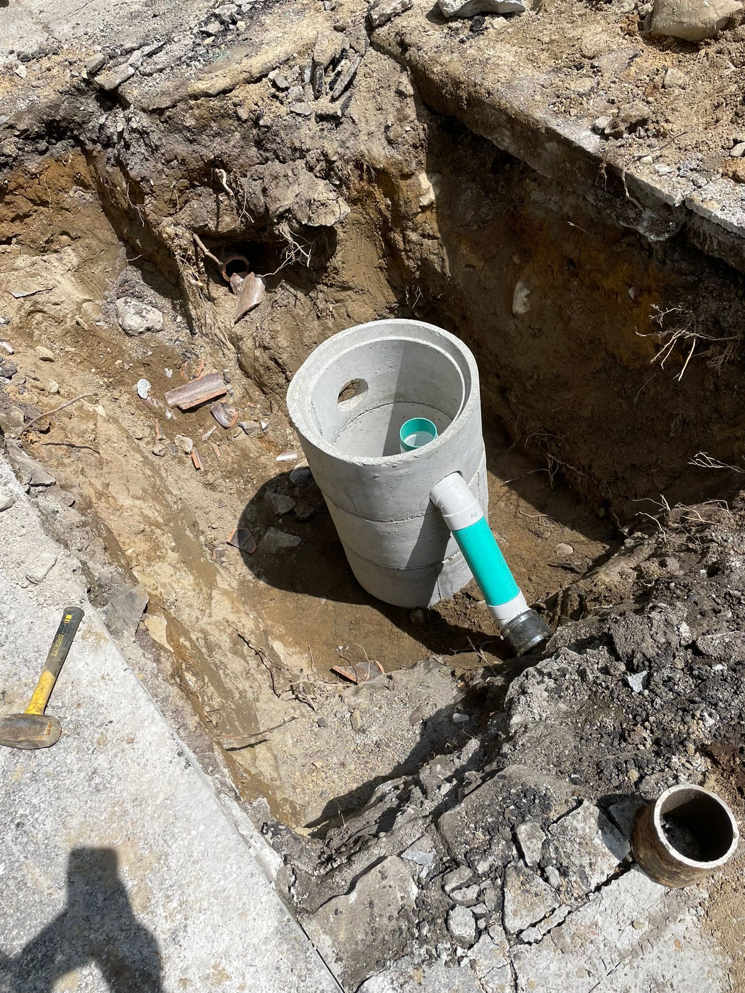 A bucket with a green handle is sitting in a hole in the ground.