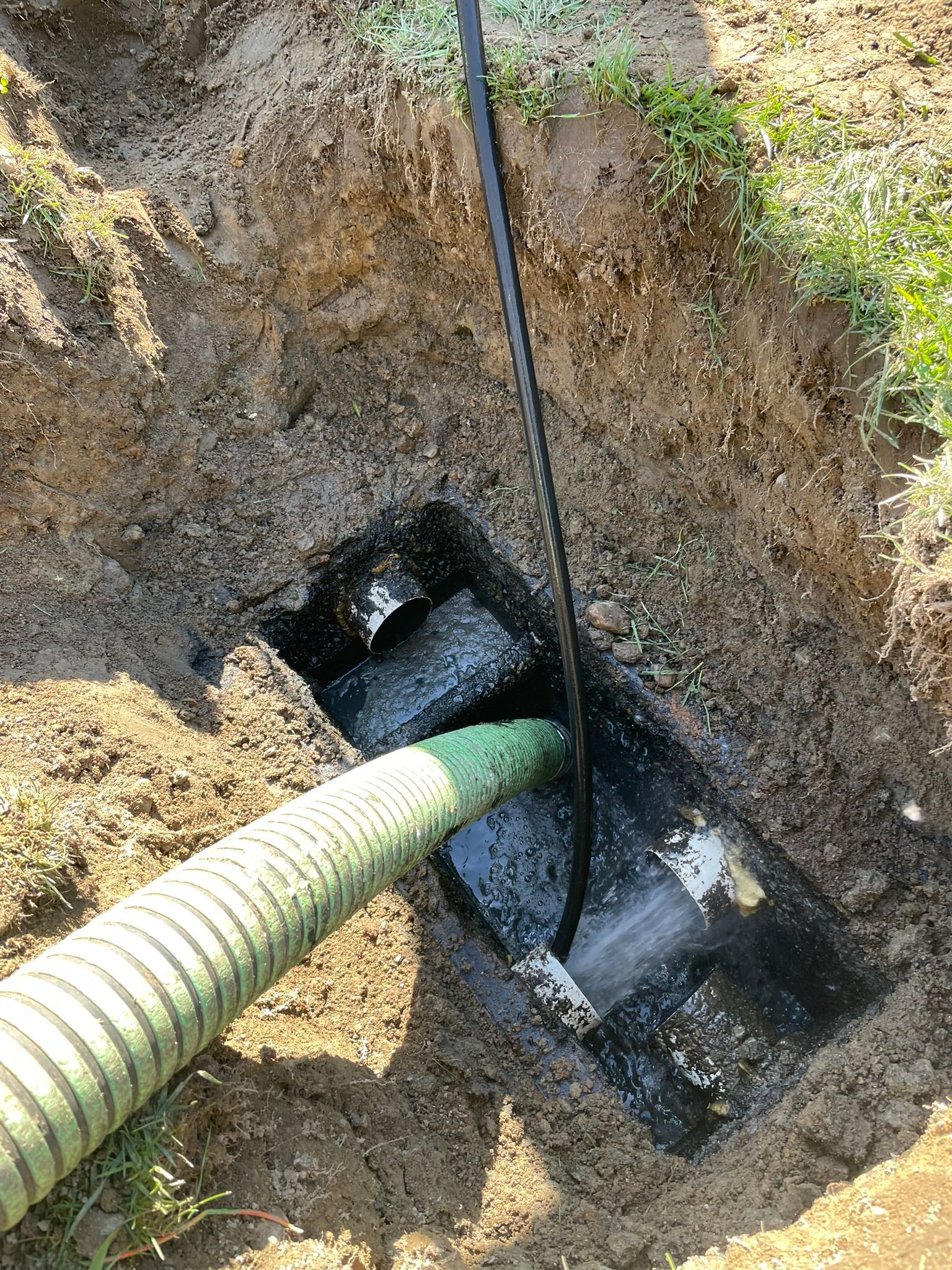 A green hose is being used to pump water into a hole in the ground.