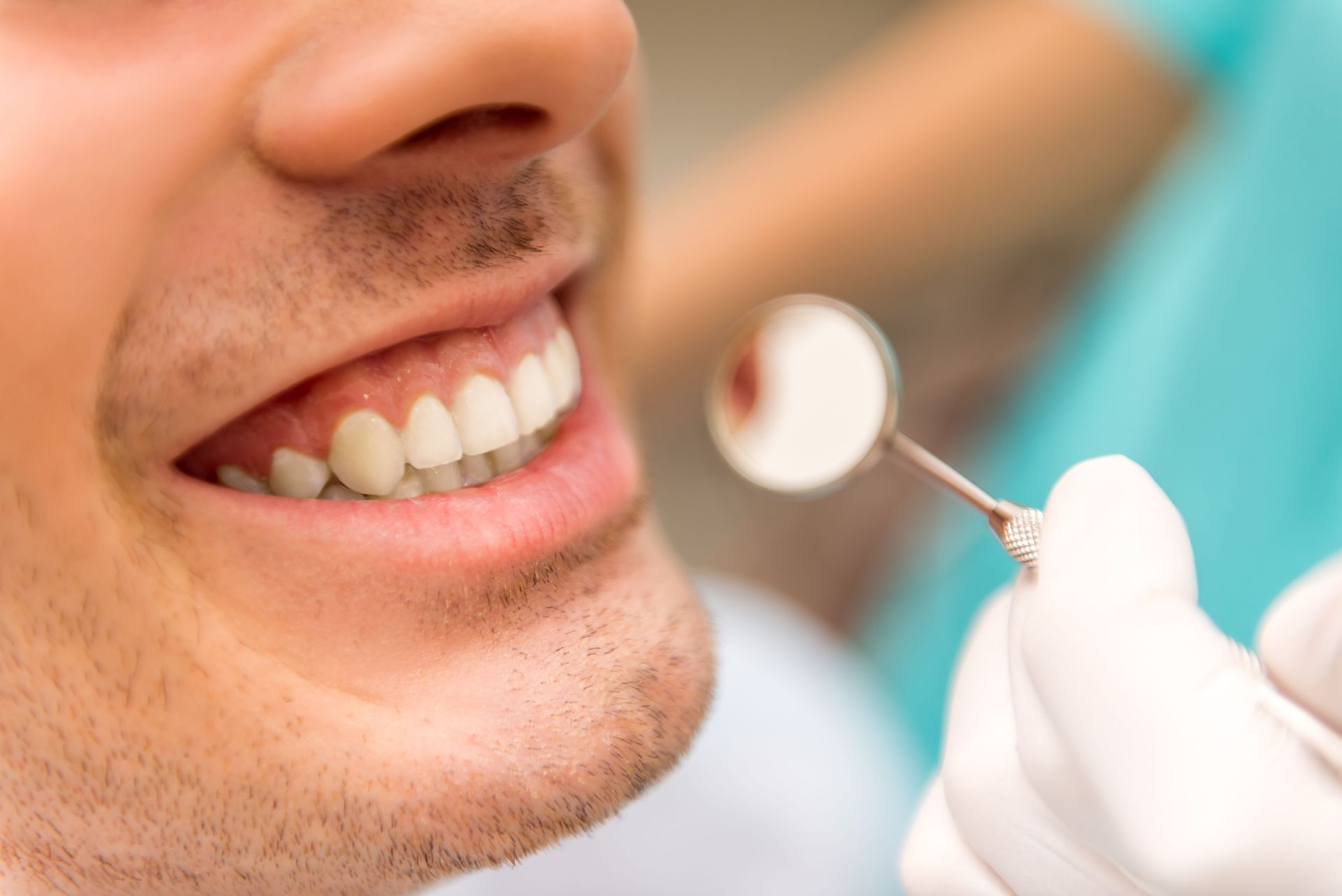 Dentist examining patient's teeth with a mirror. Patient smiling.