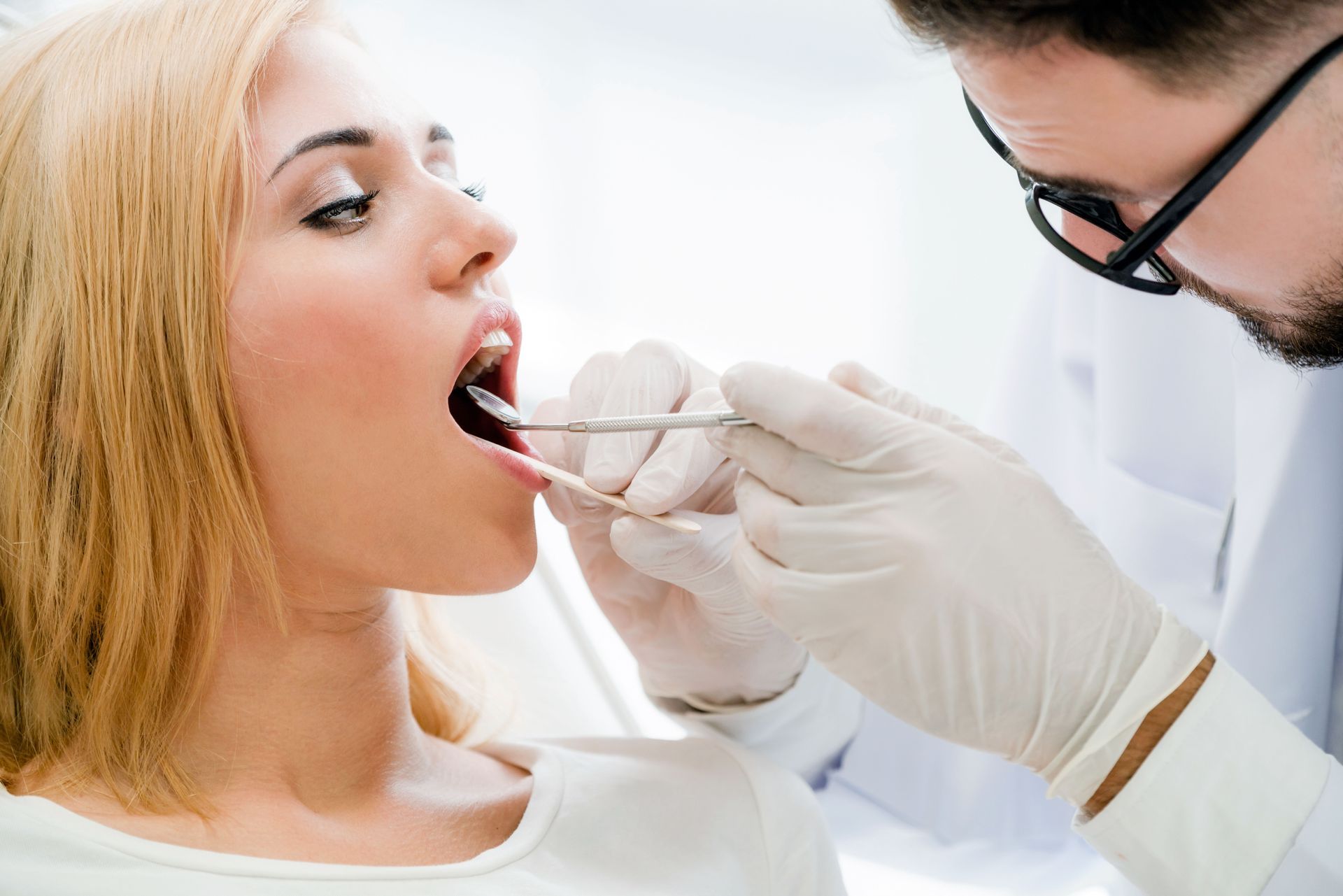 A dentist examines a patient's mouth with tools in a dental office.