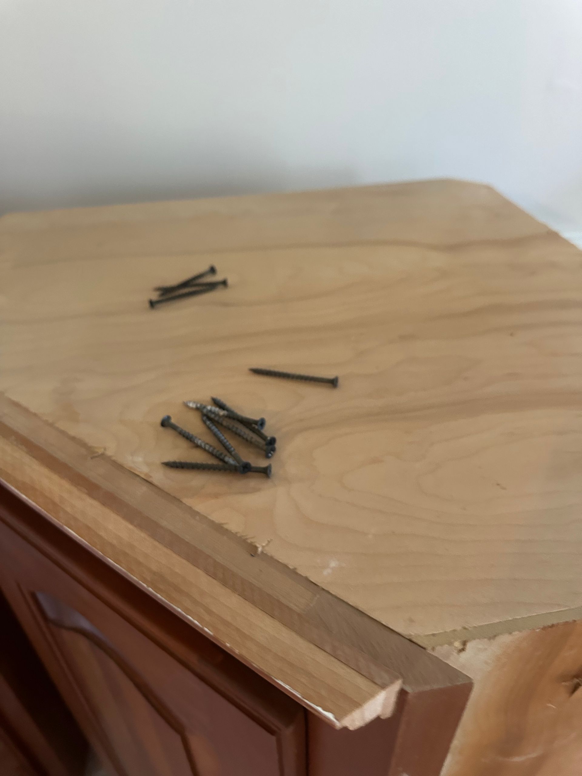 A light brown cabinet with dark screws on top. A small chip is visible on the cabinet edge.