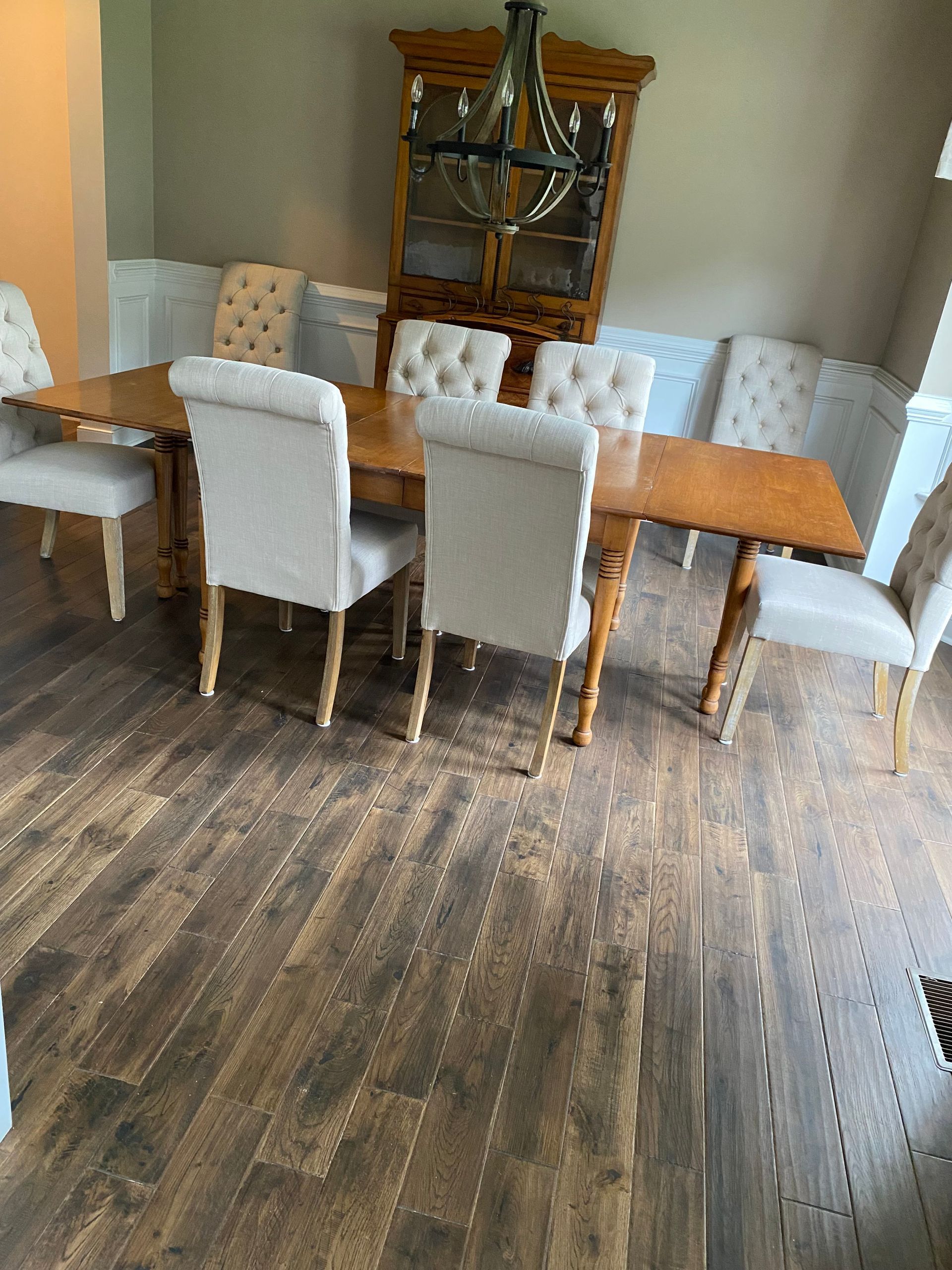 Dining room with a wooden table, upholstered chairs, and a hutch on a wood floor.