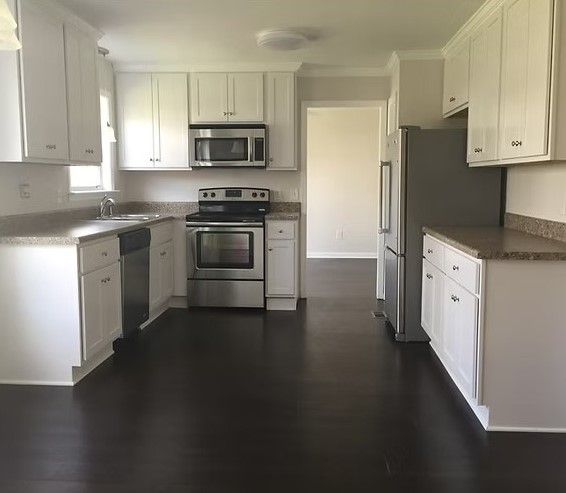White kitchen with stainless steel appliances, dark wood floor, and granite countertops.