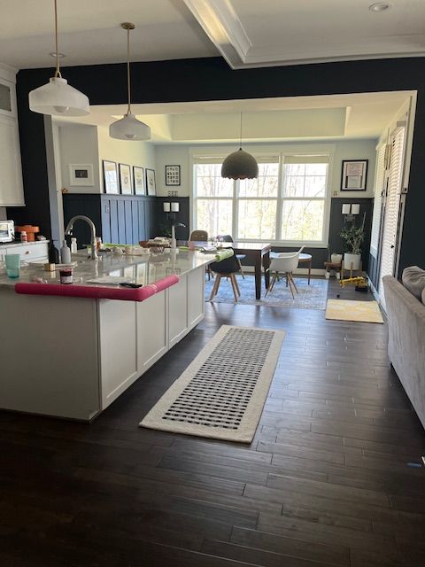 Kitchen with dark wood floors, white cabinets, navy walls, and a large island. Dining area in the background.