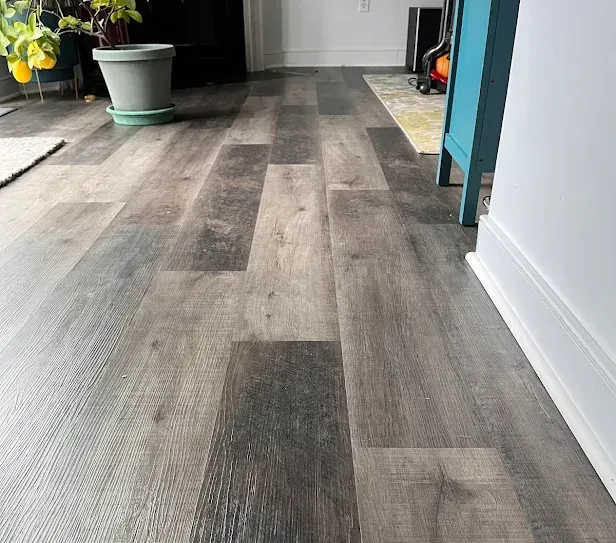 Gray wood-look flooring in a room; a plant, blue cabinet, and white wall are visible.