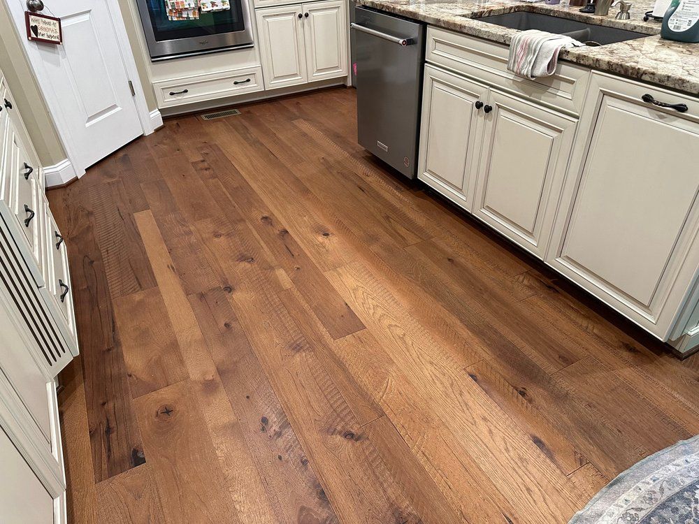 Hardwood flooring in a kitchen with white cabinets and a stainless steel dishwasher.