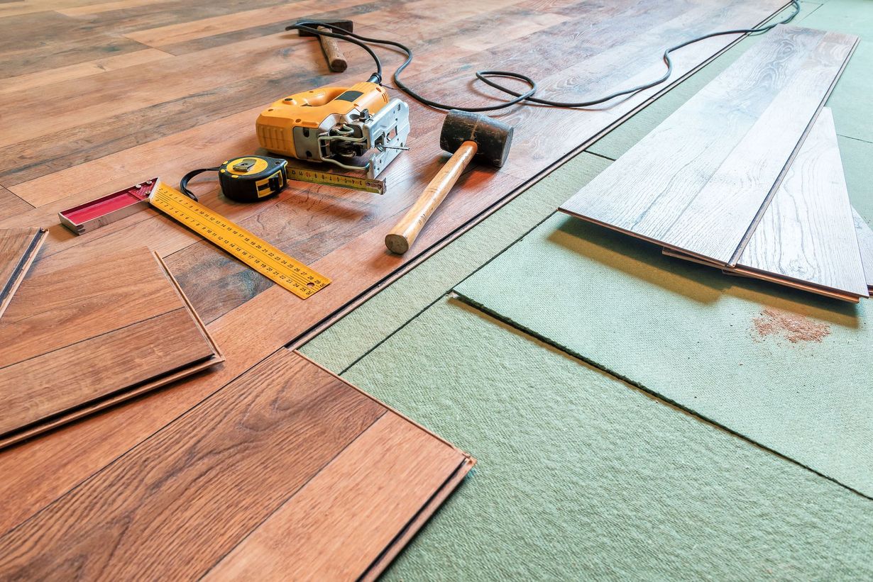 Laminate flooring installation with tools: saw, hammer, tape measure, and flooring planks.