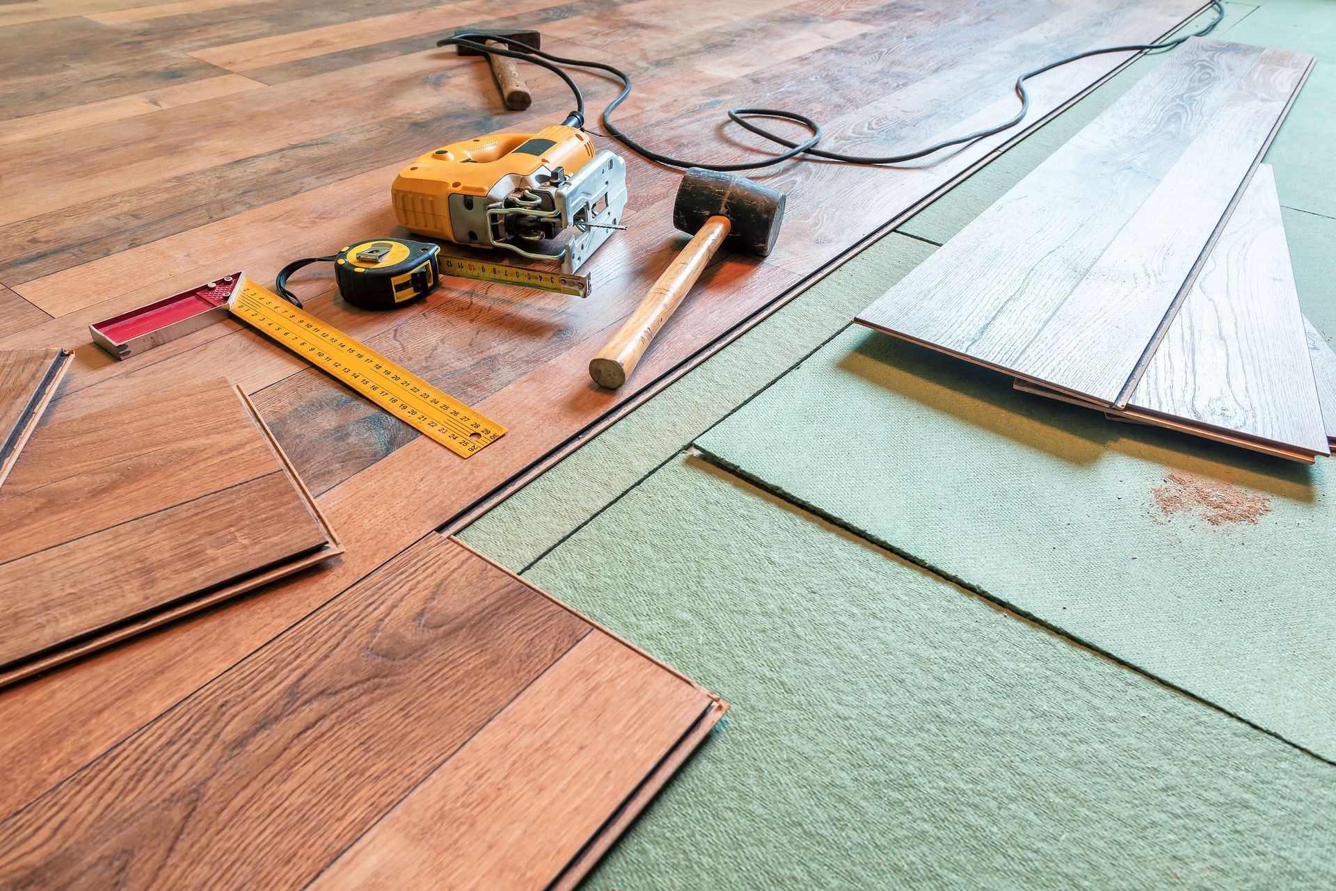 Laminate flooring installation with tools: saw, hammer, tape measure, and flooring planks.