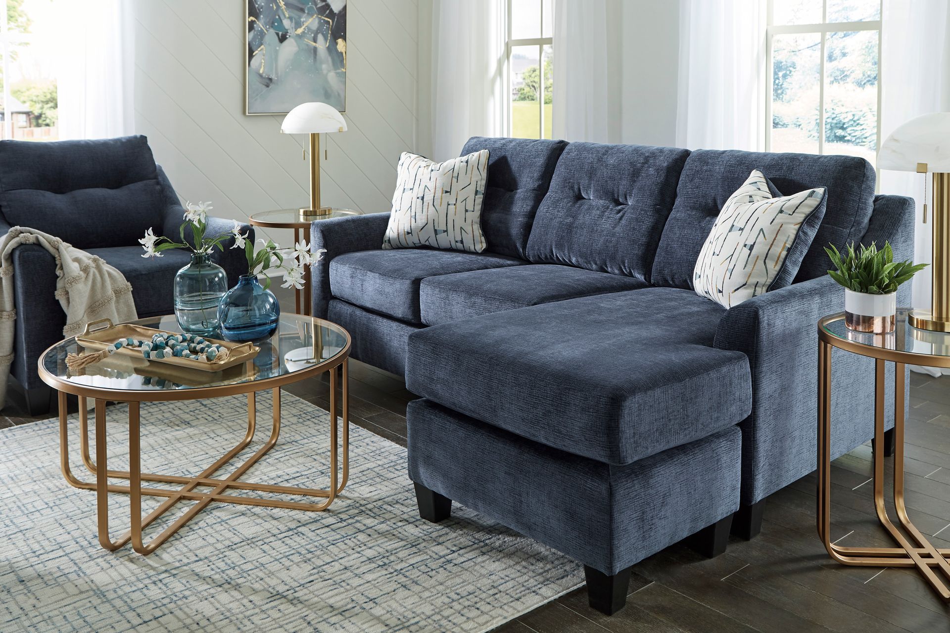 A living room with a blue sectional couch , chair , coffee table and rug.