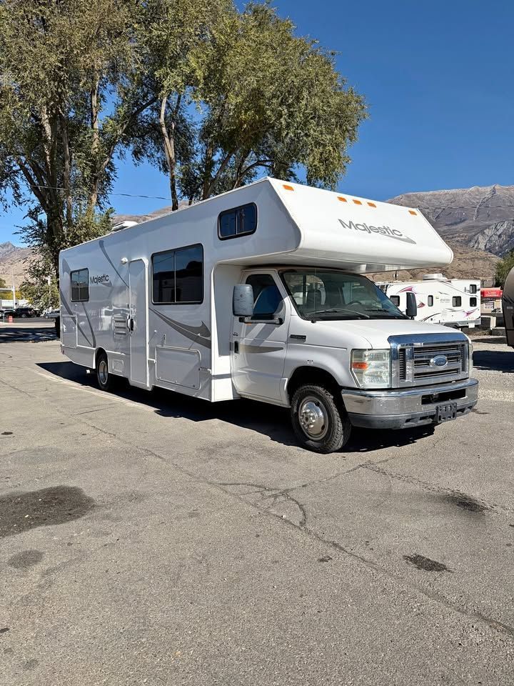 White motorhome parked on asphalt, sunny day. Trees and mountains in background.