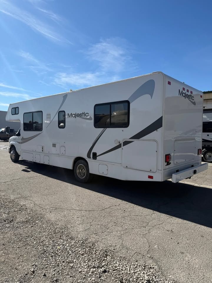 White Majestic RV parked outdoors on a gravel lot under a blue sky.