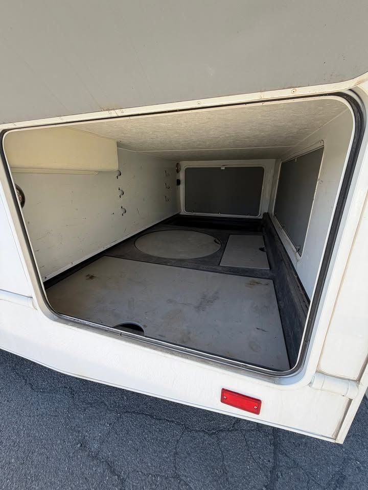 Empty RV storage compartment, open door, off-white interior, dark floor, black trim.