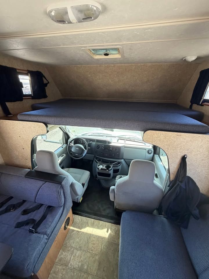 Interior of a camper van with a bed above the driver's area, seating, and a driver's seat.