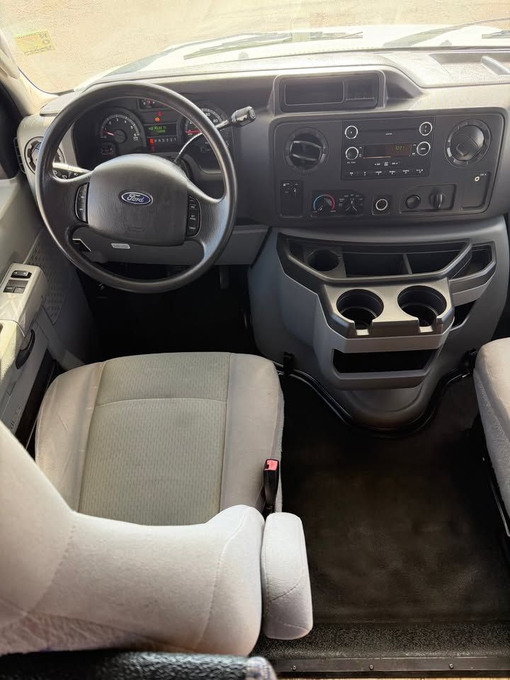 Interior of a Ford van with gray seats, black dashboard, steering wheel, and cup holders.
