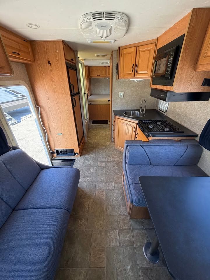 Interior of a camper with blue seating, kitchen with microwave, and wood cabinets. Open door to the left.