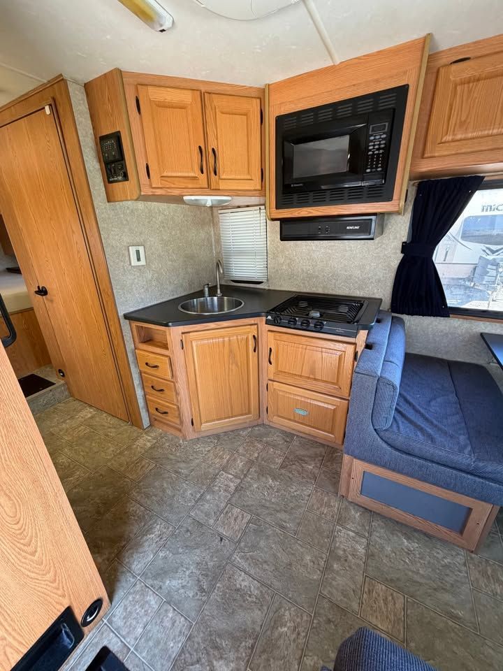 Interior of a camper with a kitchen area. Includes cabinets, microwave, stove, sink, and a seating area.