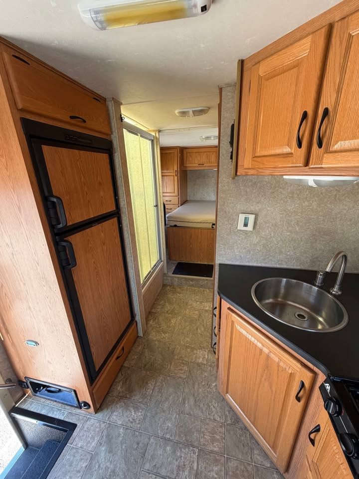 Interior of a recreational vehicle with a refrigerator, cabinets, and a kitchen sink.