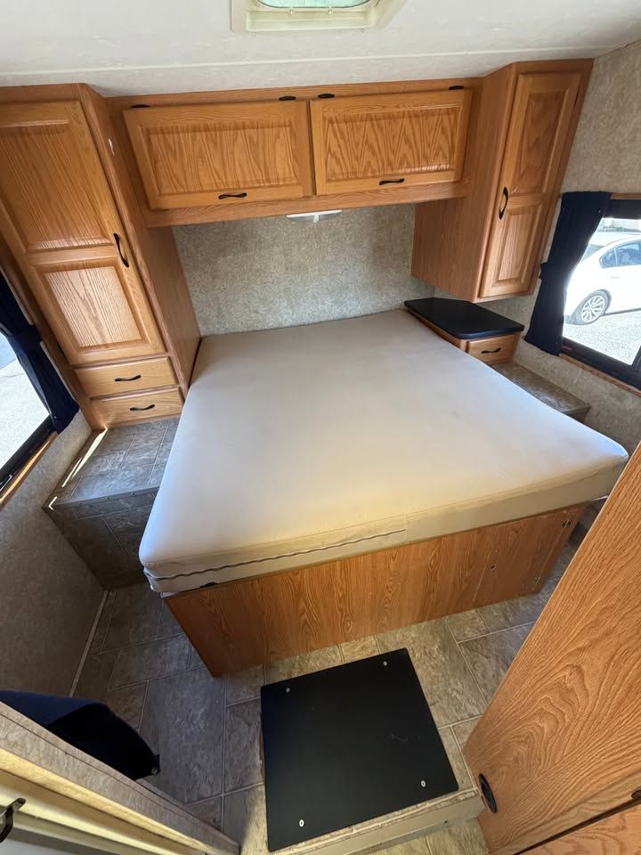 Bedroom in a recreational vehicle with overhead cabinets, bed, and storage.