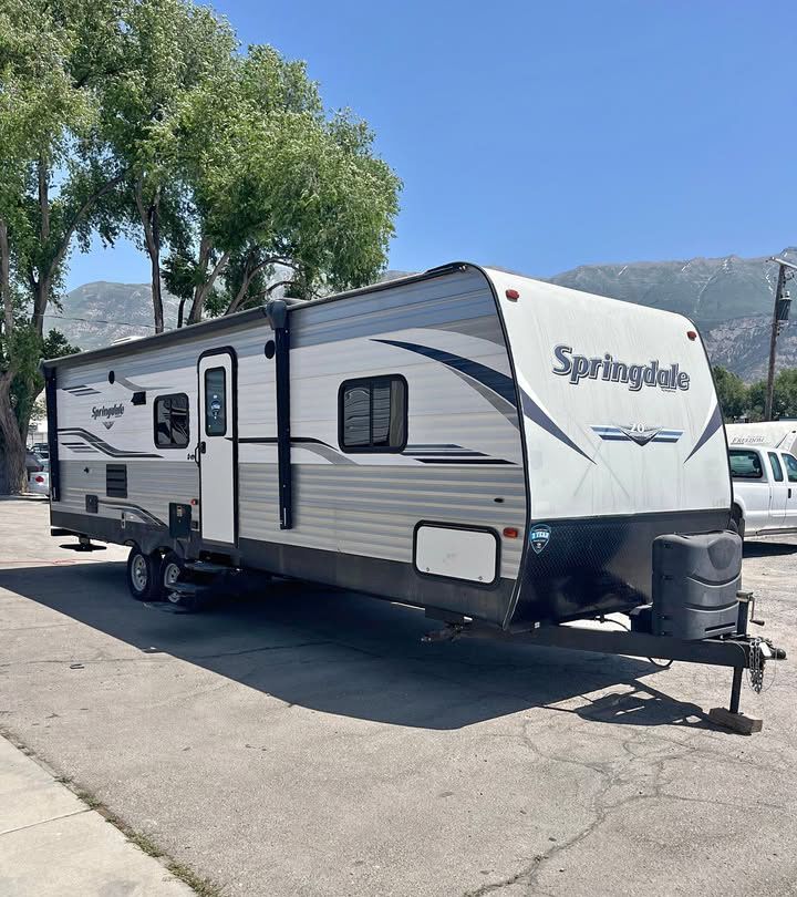 Gray and white Keystone Springdale travel trailer parked on asphalt, daytime.