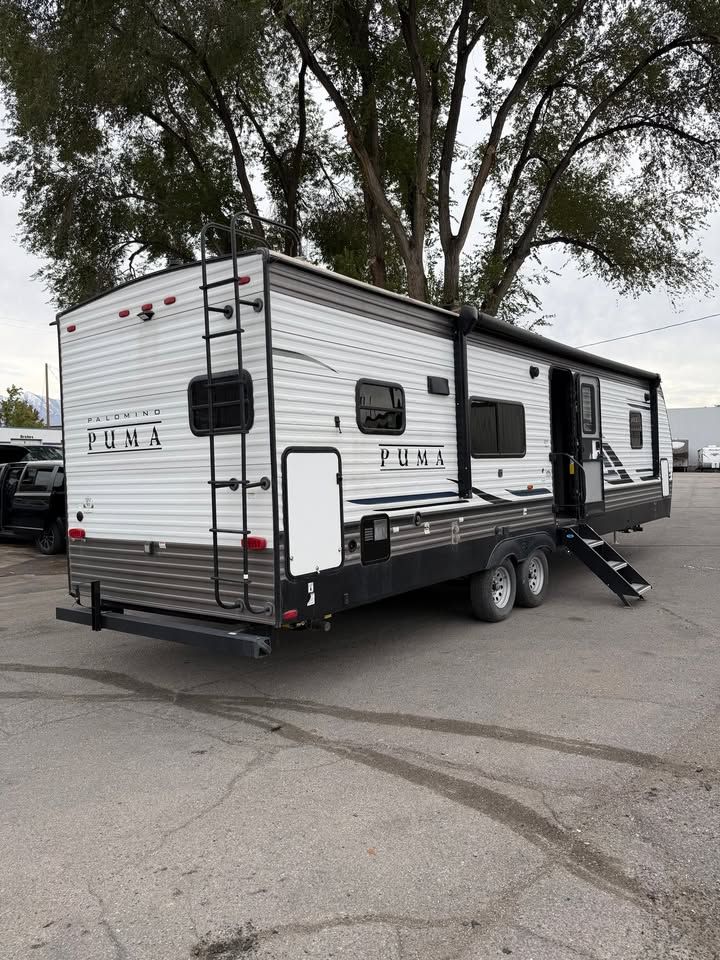 White and brown Puma travel trailer parked outdoors with ladder and awning extended.