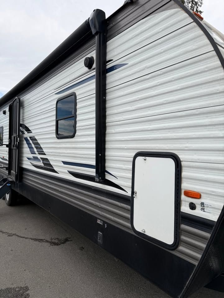RV with white and gray corrugated siding, black awning, and storage door.