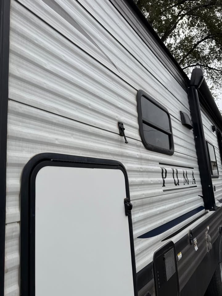 Side view of a white and gray Puma travel trailer, with a door and small window visible.